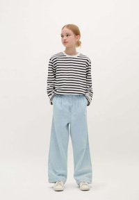 Pasiasty czarno-biały longsleeve połączony z jasnoniebieskimi szerokimi spodniami. Białe trampki dopełniają stylizację.