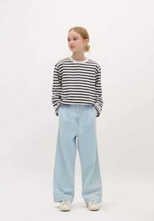Gestreepte zwart-witte langemouwen top gecombineerd met lichtblauwe wide-leg broek. Witte sneakers maken de outfit compleet.