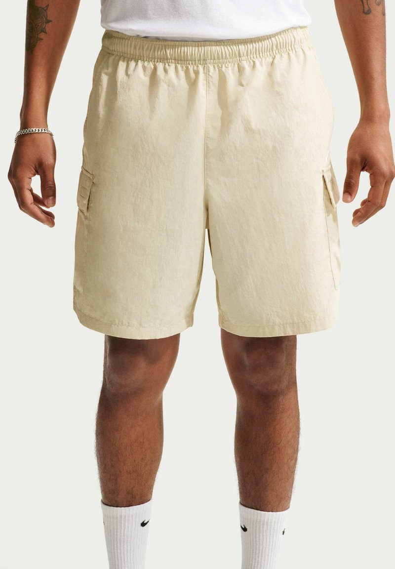 Shorts cargo beiges avec une ceinture élastique, deux poches latérales et une poche latérale à rabat. Confectionnés en tissu léger avec une finition texturée.