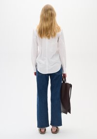 Biała koszula z długim rękawem, niebieskie szerokie dżinsy, brązowa torba na ramię, zestawione z beżowymi butami wsuwanymi. Prosty design, jednolite kolory.