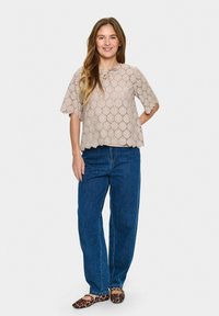 Top in pizzo beige con orlo a onde, maniche corte e scollo rotondo. Abbinato a jeans blu a gamba dritta e ballerine con stampa leopardata.