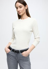 Soonikkoes kreemjas pika varrukaga särk ümmarguse kaelusega, mida on kombineeritud hallide teksade ja musta vöös, millel on hõbedane pandlaga. Lame tekstuur, keha järgiva lõikega.