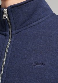 Giacca zip-up blu navy realizzata in tessuto morbido con colletto alto. Presenta una zip argentata e un logo in rilievo sul petto.