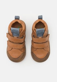 Bruine peuterschoenen met twee klittenbandsluitingen, blauwe trekkoorden en ronde rubberen zolen op een witte achtergrond.