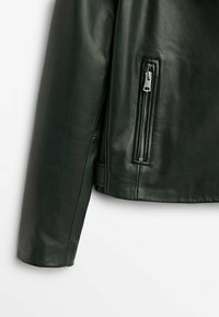 Manche de veste en cuir noir avec une poche verticale zippée près de l'ourlet sur un fond blanc uni.