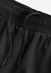 Svarta atletiska shorts med elastisk midja, med en r gathered-textur och släta svarta dragsnoddar för justering. Slät tygtextur.