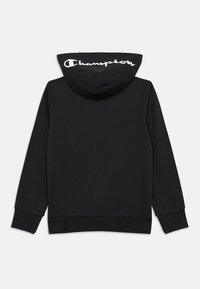 Černá mikina s kapucí s velkým bílým logem "Champion" na zadní straně, vyrobená z měkké látky s volným střihem a klokankovou kapsou.