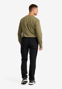 Long-sleeve olive green shirt paired with black pants. The pants have an elastic waistband and side pockets. White and black sneakers.