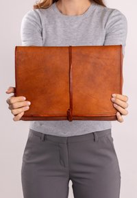 Hnědý kožený obal na tablet s hladkou texturou, minimalistickým designem a centrálním koženým popruhem pro uzavření.