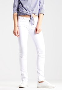 Jeans ajustados blancos de mezclilla, con un clásico diseño de cinco bolsillos. Combinados con una camisa de rayas azul y blanca anudada a la cintura.