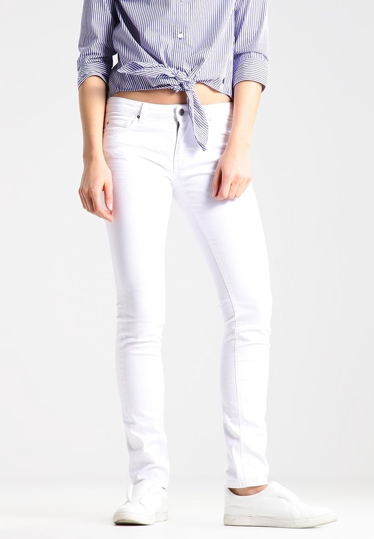 Jeans ajustados blancos de mezclilla, con un clásico diseño de cinco bolsillos. Combinados con una camisa de rayas azul y blanca anudada a la cintura.