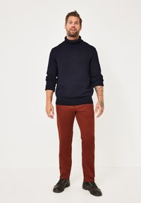 Navy knit turtleneck sweater with ribbed cuffs, paired with rust-colored slim-fit trousers and black lace-up boots.