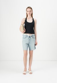 Black sleeveless top, light blue denim shorts with frayed hem, white drawstring, holding a textured gold-colored handbag, wearing beige sandals.