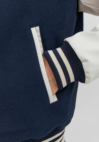 Marineblauwe jas met textuurstof, een witte leren mouw, gestreepte ribbelsokjes en een ontwerp met zijzakken.