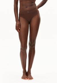 Bruine slip met hoge taille gemaakt van gladde stof met een brede elastische tailleband met een discreet logo. Getoond op een model met blote voeten.