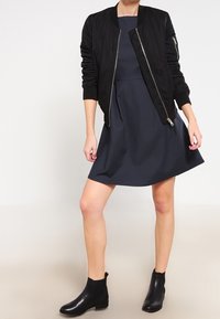 Svart bomberjacka, åtsittande marinblå klänning och svarta ankelboots. Jackan har dragkedjor och klänningen har en utsvängd kjoldesign.