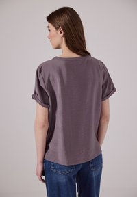 Blůza s krátkým rukávem a volným střihem v světlé mauve, s jemnou texturou a kulatým výstřihem, v kombinaci s klasickými modrými džíny.