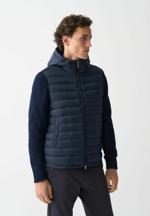 Navy hooded jacket with quilted front and ribbed sleeves, featuring a zip closure and side pockets. Smooth texture and structured design.