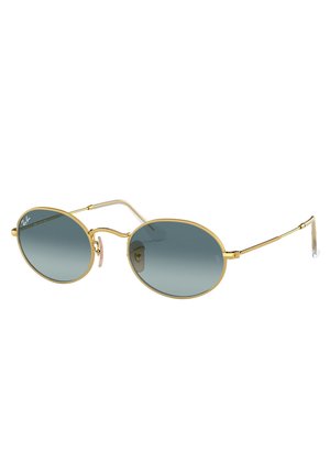 Occhiali da sole ovali con montatura in metallo dorato, lenti blu sfumate e aste sottili. Dettagli caratteristici includono pastiglie nasali rosa e un bordo testurizzato.