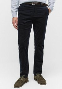 Marina blåa kordflossbyxor med rak passform och subtil textur, ihop med ett flätat brunt läderbälte och bruna mockaskor.