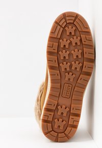 Schoen met rubberen zool en een bruine, zachte bovenzijde, voorzien van een gestructureerde buitenzool met gripjes en een logo nabij de hiel.