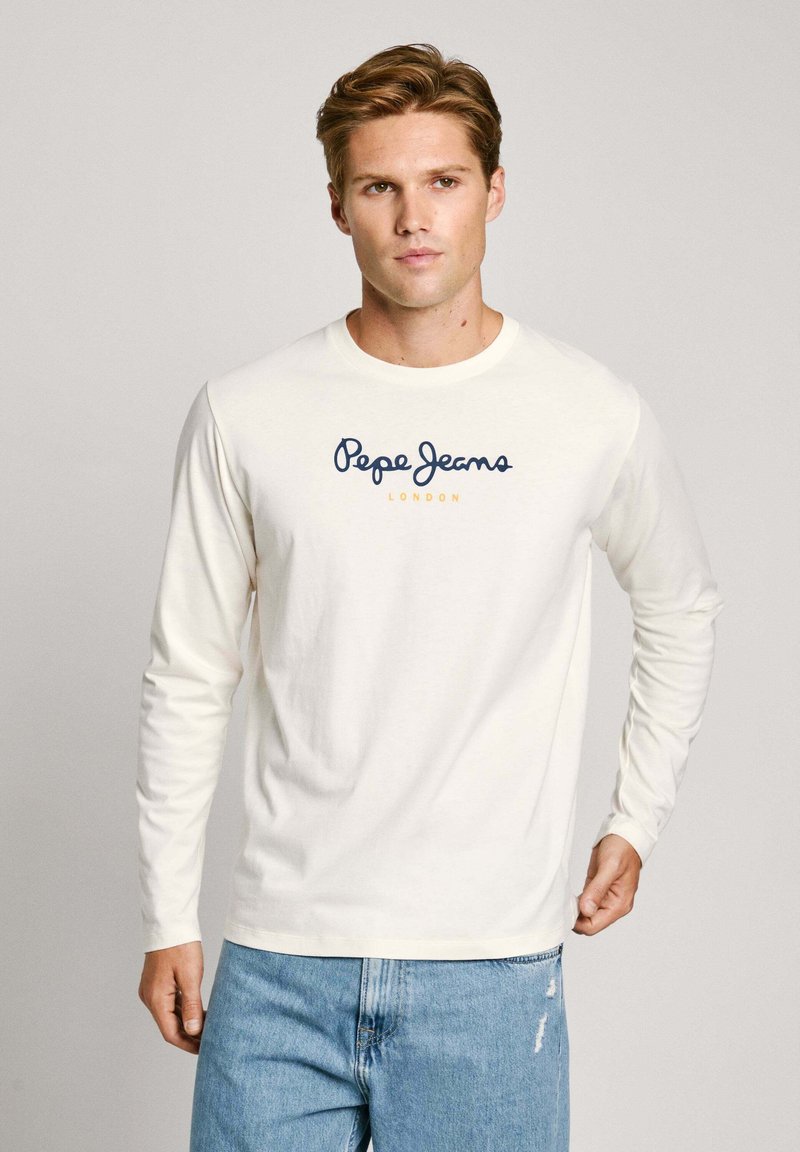 Langärmliges cremefarbenes Hemd mit Rundhalsausschnitt, versehen mit einem marineblauen "Pepe Jeans"-Logo und dem Schriftzug "LONDON" in Gelb. Getragen mit hellblauen Jeans.