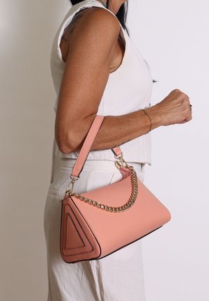 Borsa in pelle rosa con un design triangolare, superficie texturizzata, accentuata da una catena dorata e una tracolla removibile, tenuta contro uno sfondo bianco.