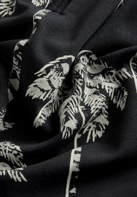 Țesătură neagră cu un model botanic alb, cu frunze și ramuri, având o textură delicată și o cădere netedă.