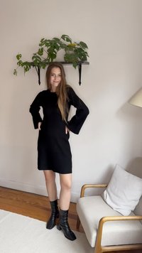 Vestido de malha preto canelado com mangas longas, apresentando um silhueta ajustada. Combinado com botas pretas de salto alto até ao joelho. Design simples e elegante.