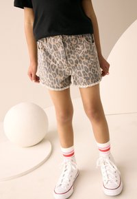 Jeans kratke hlače s leopardjim vzorcem in raztrganim robom, nošene s belimi supergami in črtastimi nogavicami. Preprosta črna majica združena z nevtralnim ozadjem.