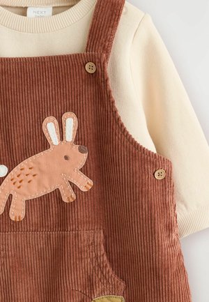 Rust-colored corduroy overalls with a rabbit applique, featuring wooden buttons and a cream long-sleeve top underneath.