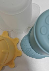 Drie siliconen babyfles spenen met ronde bodems in geel, wit en blauw op een witte ondergrond.