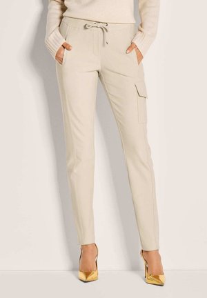 Beige Kordelhosen mit slim-fit, seitlichen Taschen und Cargo-Taschen-Details. Weicher Stoff mit flachen Nähten, kombiniert mit goldenen High Heels.