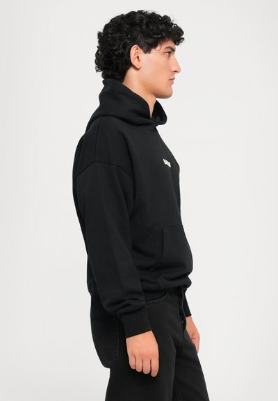Sudadera con capucha negra fabricada en un material suave, con un bolsillo canguro y un logo minimalista en el pecho. Ajuste casual, mangas largas.
