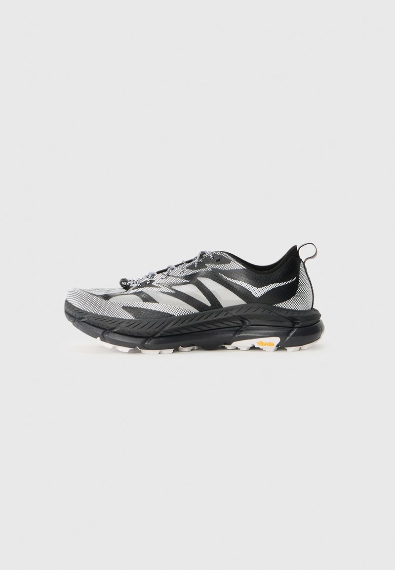 Chaussure de course athlétique noir et blanc avec tige en mesh, côtés à motifs, semelle épaisse et boucle au talon.