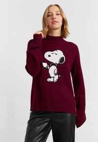 Burgunderfarbener Pullover aus Strickmaterial mit hohem Kragen, versehen mit einem schwarz-weißen Snoopy-Motiv auf der Vorderseite. Gerippter Saum und Bündchen.