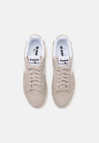 Beige suede sneakers with white accents, round toe, and perforation details. Features lace-up closure and a logoed insole.