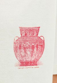 Rood gedecoreerde aardewerken vaas op een gestructureerde witte stoffen achtergrond, met gedetailleerde patronen en twee zijhandvatten.