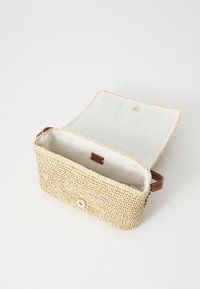 Woven straw bag with a beige exterior, leather accents, and a button closure. Features a light interior and a small label inside.