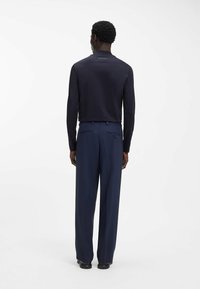 Marineblaue Langarmbluse mit hohem Kragen; kombiniert mit marineblauen Hosen mit Gesäßtaschen und feiner Textur; durchgehend einfarbig.