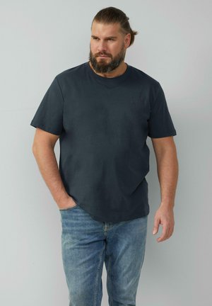 Czarny t-shirt z bawełny w kolorze ciemnoszarym, z okrągłym dekoltem, krótkimi rękawami i luźnym krojem. Noszony z jasnoniebieskimi dżinsami.