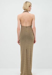 Robe à col halter en tissu métallique doré avec un design dos nu, une silhouette ajustée et une légère fente à l'ourlet.