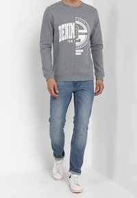 Sudadera de algodón gris con texto gráfico blanco, combinada con jeans de denim azul claro y zapatillas blancas. Ajuste casual y cuello redondo.