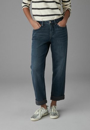 Donkerblauwe denim jeans met een ontspannen pasvorm, omgeslagen bij de enkels, met voorzakken en een klassieke knoopsluiting. Gemaakt met een wit gestreepte shirt en sneakers.