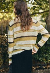 Maglione a righe in morbido knit con strisce gialle, bianche e marroni, con una vestibilità leggermente oversize e polsini a costine. Gonna nera sotto.