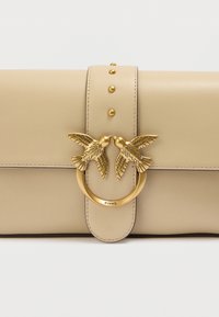 Μπεζ δερμάτινη τσάντα με δομημένο σχέδιο. Διαθέτει χρυσούς μεταλλικούς διακοσμητικούς κρίκους σε σχήμα πουλιών, τρουκς και κεντρικό κούμπωμα.