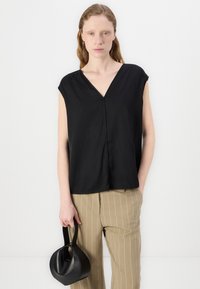Black sleeveless top with a V-neck, featuring draped fabric. Paired with high-waisted striped beige pants and a round black handbag.
