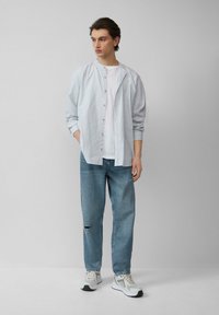 Pasiasta koszula w kolorze jasnoniebieskim i białym, noszona na białej koszulce. Uzupełniona zniszczonymi jasnoniebieskimi dżinsami i szarymi trampkami.