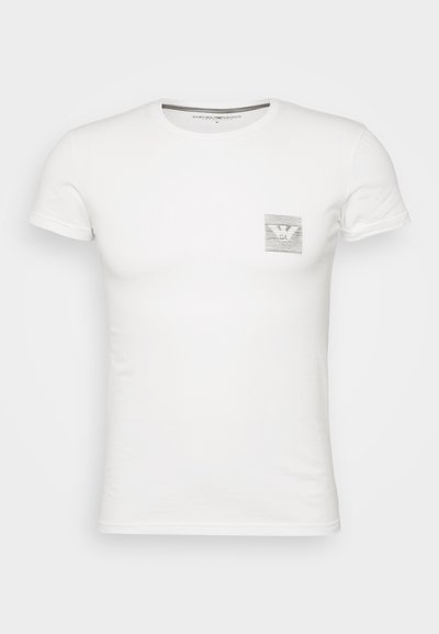 Λευκό κοντομάνικο μπλουζάκι από βαμβάκι, με μικρό γκρι γραφικό σχέδιο τσέπης που περιλαμβάνει ένα λογότυπο αετού στην αριστερή περιοχή του στήθους.