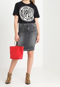 Černé tričko s logem a bílým potiskem, šedá džínová tužková sukně, červená kabelka s kulatým uchem a kotníkové boty s hadím vzorem.